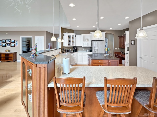 kitchen featuring recessed lighting, white appliances, glass insert cabinets, and a kitchen breakfast bar