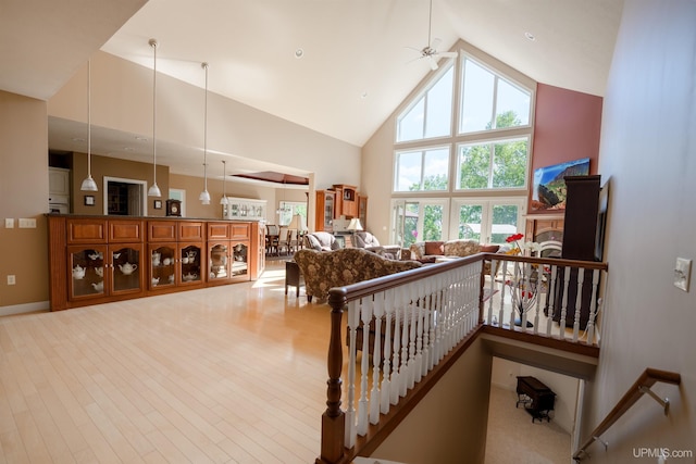 interior space with baseboards, a fireplace, ceiling fan, high vaulted ceiling, and wood finished floors