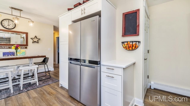 kitchen with white cabinetry, baseboard heating, wood finished floors, and stainless steel appliances