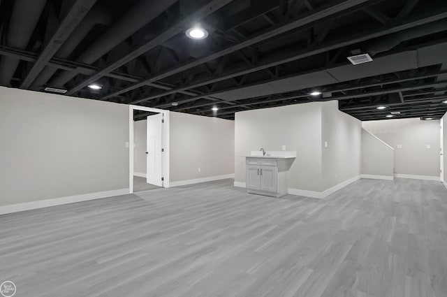 finished below grade area featuring wood finished floors, baseboards, indoor wet bar, and a sink