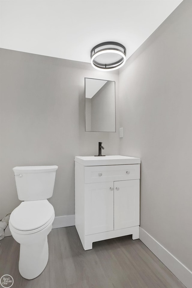 half bathroom featuring baseboards, wood finished floors, vanity, and toilet