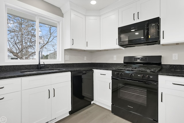 kitchen featuring white cabinets, light wood finished floors, dark stone countertops, a sink, and black appliances