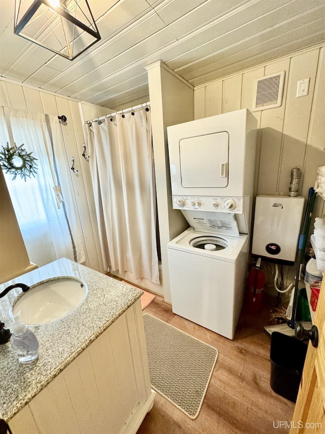bathroom featuring a shower with curtain, visible vents, wood finished floors, a sink, and stacked washing maching and dryer