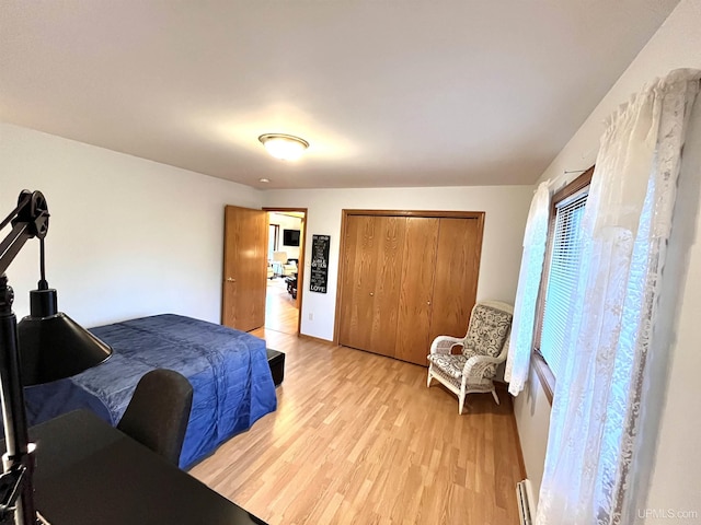 bedroom featuring a baseboard heating unit, a closet, and light wood-style flooring