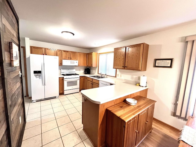 kitchen with a sink, light countertops, white appliances, a peninsula, and brown cabinetry