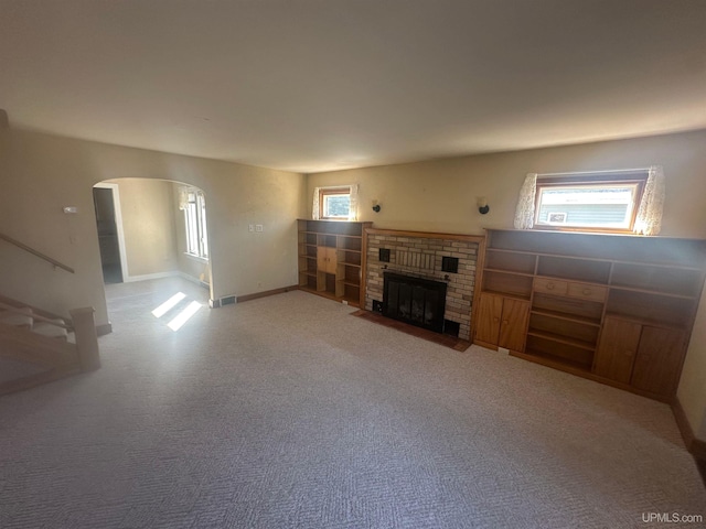 unfurnished living room featuring visible vents, baseboards, arched walkways, a fireplace, and carpet flooring