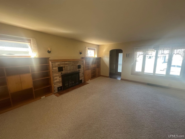 unfurnished living room featuring carpet flooring, baseboards, arched walkways, and a fireplace