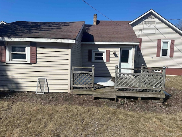 back of property with roof with shingles, a deck, and a chimney