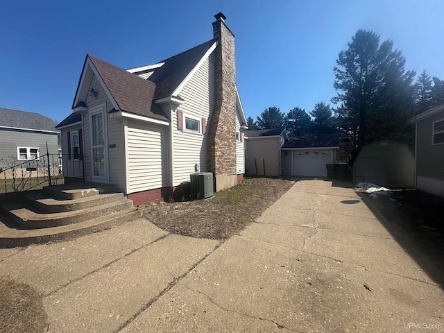 view of side of property featuring concrete driveway, central air condition unit, an outdoor structure, a chimney, and a garage