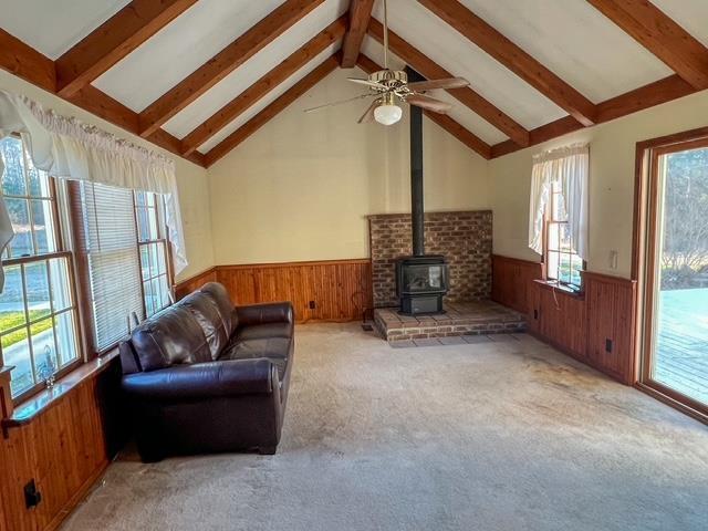 carpeted living room with wainscoting, wood walls, beam ceiling, and a wood stove