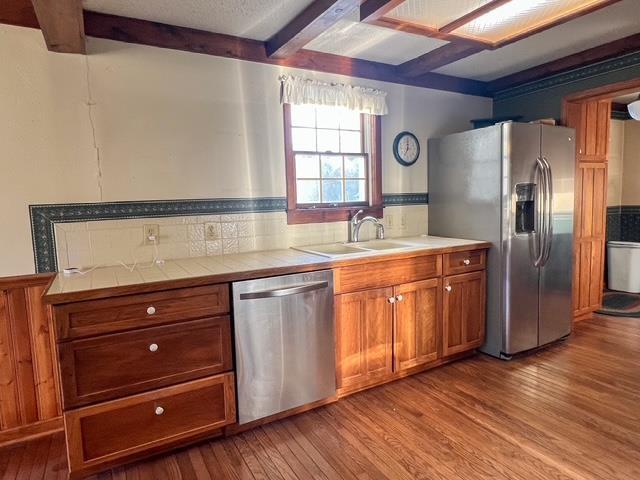 kitchen with stainless steel appliances, light wood-style flooring, a sink, brown cabinetry, and tile countertops