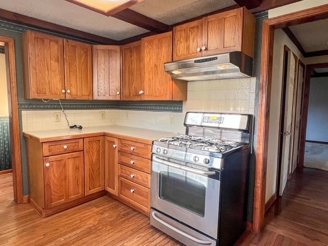 kitchen with brown cabinets, under cabinet range hood, light wood-style floors, and stainless steel gas stove