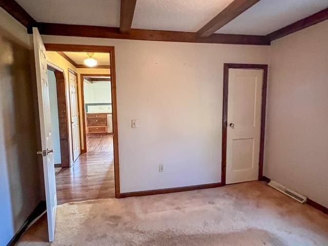 carpeted empty room with baseboards, beam ceiling, and visible vents