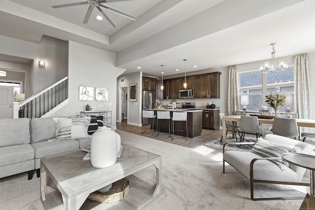 living area featuring ceiling fan with notable chandelier, recessed lighting, light wood-style floors, and stairs