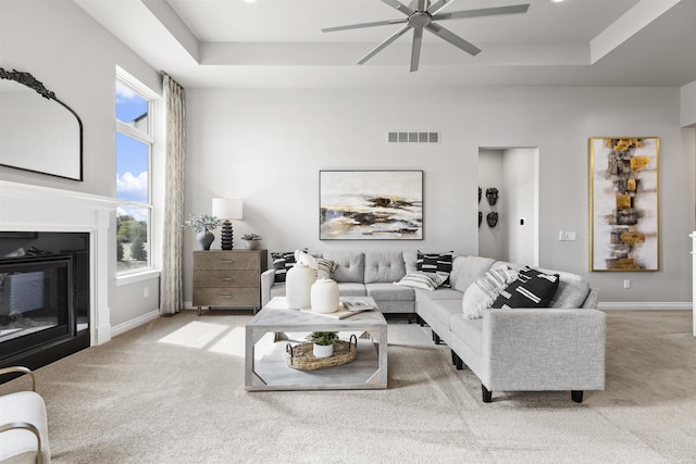 living area featuring a tray ceiling, visible vents, a ceiling fan, and light carpet