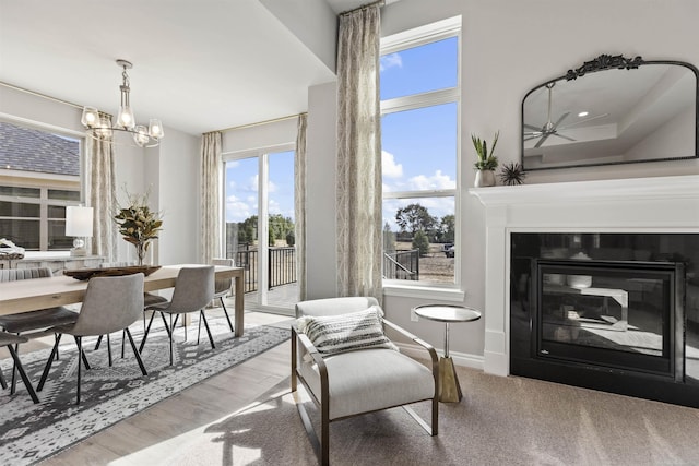 living area featuring a glass covered fireplace, wood finished floors, baseboards, and an inviting chandelier