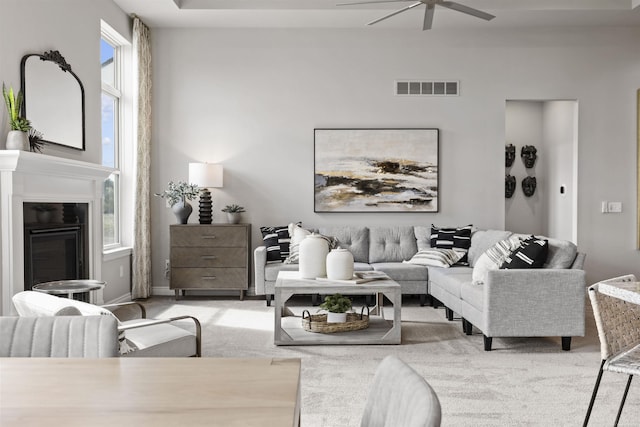 living room featuring ceiling fan, light carpet, a glass covered fireplace, and visible vents
