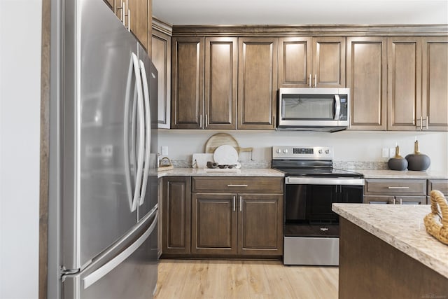 kitchen with light wood-style floors, light stone countertops, dark brown cabinetry, and stainless steel appliances