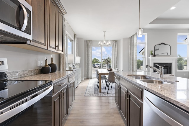 kitchen with a sink, a healthy amount of sunlight, a glass covered fireplace, a chandelier, and appliances with stainless steel finishes