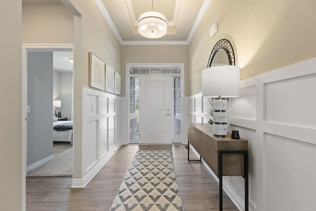 foyer entrance with a decorative wall, crown molding, wood finished floors, and a raised ceiling