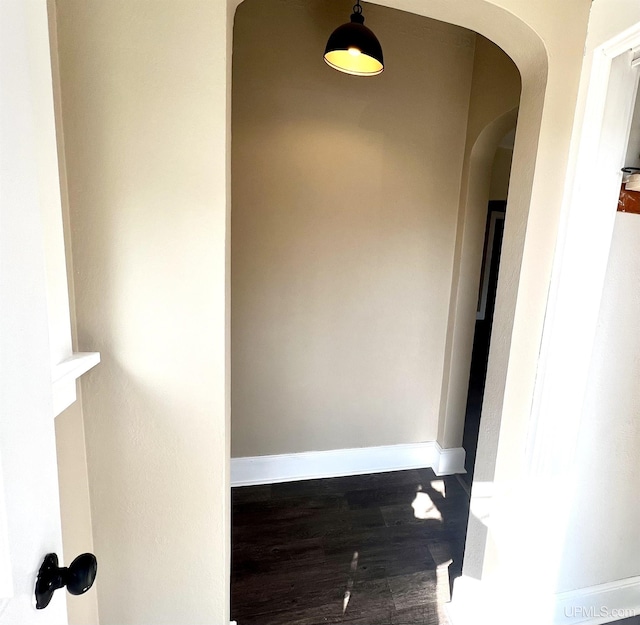 hall with arched walkways, wood finished floors, and baseboards