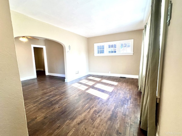 spare room with visible vents, a ceiling fan, dark wood-type flooring, arched walkways, and baseboards