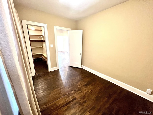 unfurnished bedroom featuring a walk in closet, dark wood finished floors, and baseboards