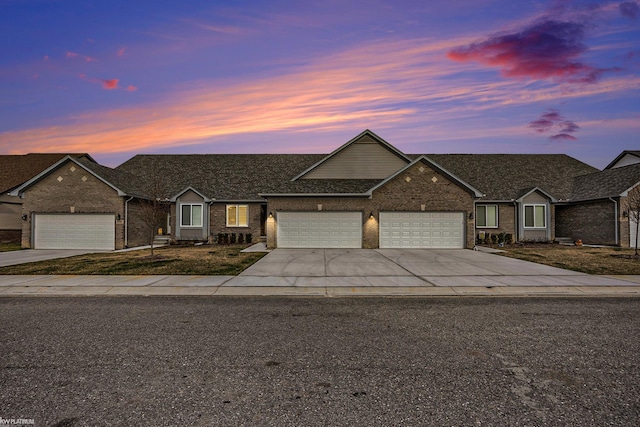view of front of property featuring an attached garage, a shingled roof, brick siding, and concrete driveway