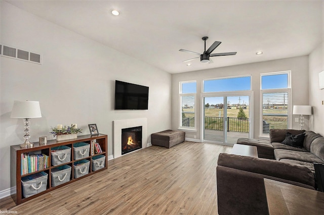 living room featuring a glass covered fireplace, wood finished floors, visible vents, and a ceiling fan
