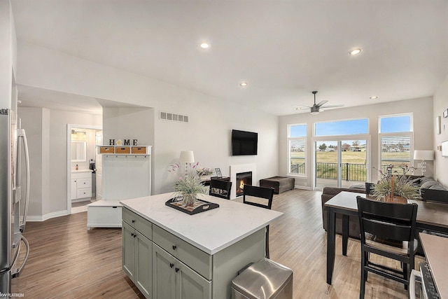 kitchen with a warm lit fireplace, visible vents, a ceiling fan, freestanding refrigerator, and open floor plan