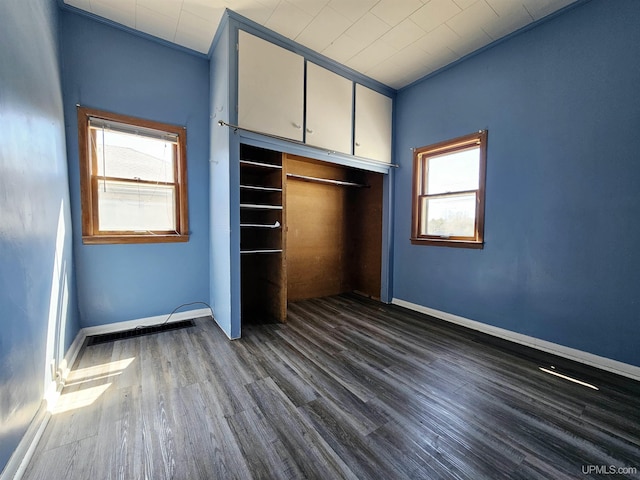 unfurnished bedroom with baseboards, dark wood-type flooring, and multiple windows