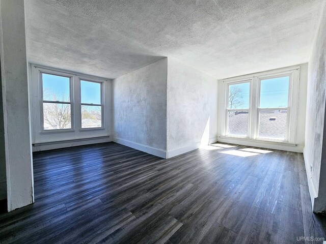unfurnished room featuring a baseboard heating unit, dark wood finished floors, baseboards, and a textured ceiling