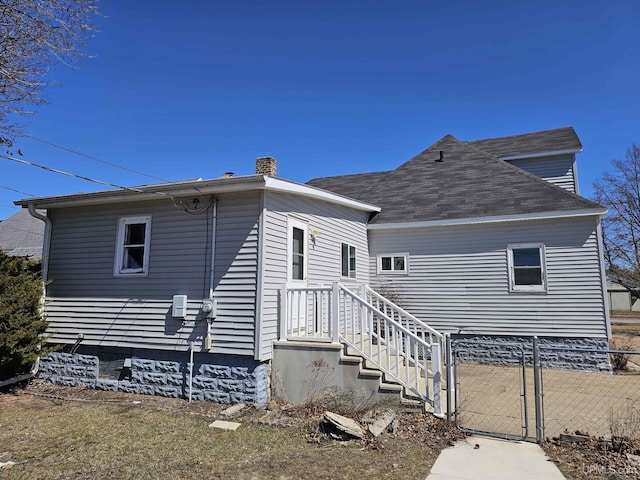 back of house with fence, a chimney, and a gate
