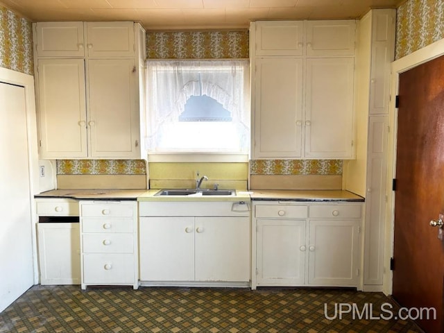 kitchen featuring wallpapered walls, a sink, and white cabinetry