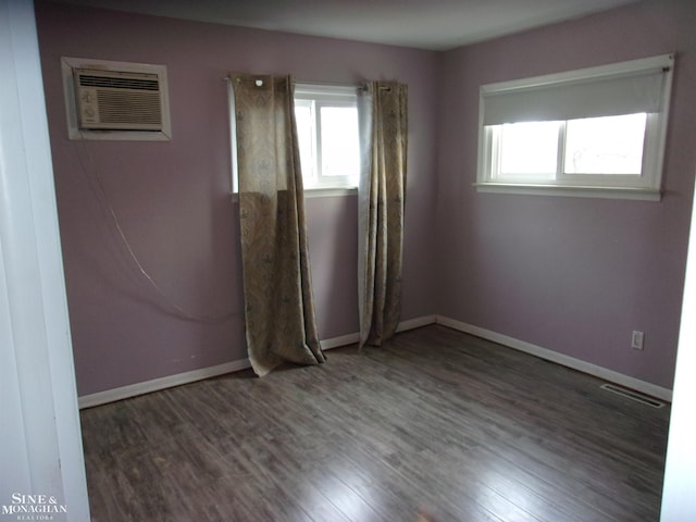 unfurnished room featuring wood finished floors, visible vents, a wall unit AC, and a wealth of natural light