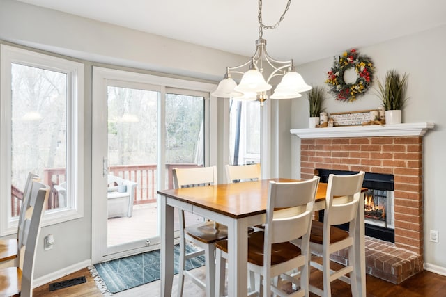 dining room with visible vents, baseboards, a notable chandelier, a brick fireplace, and wood finished floors