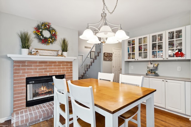 dining room with wood finished floors, stairs, an inviting chandelier, a brick fireplace, and visible vents