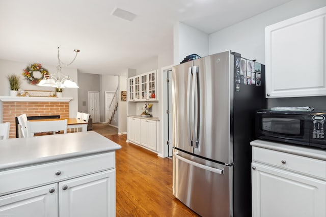kitchen with black microwave, white cabinetry, light wood finished floors, and freestanding refrigerator