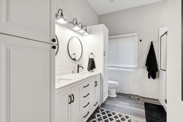 bathroom with a wainscoted wall, a sink, double vanity, toilet, and a shower stall