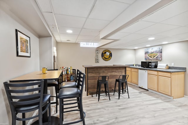 bar featuring black microwave, dishwasher, indoor bar, light wood-style flooring, and a paneled ceiling