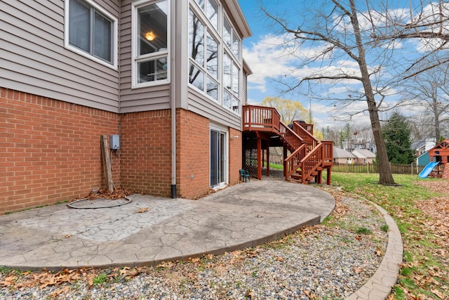 view of side of home featuring a playground, fence, brick siding, stairs, and a patio