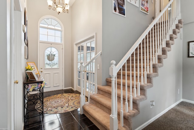 foyer entrance with baseboards, a towering ceiling, a chandelier, stairway, and dark tile patterned floors