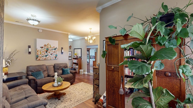 living area with a chandelier, wood finished floors, visible vents, and crown molding