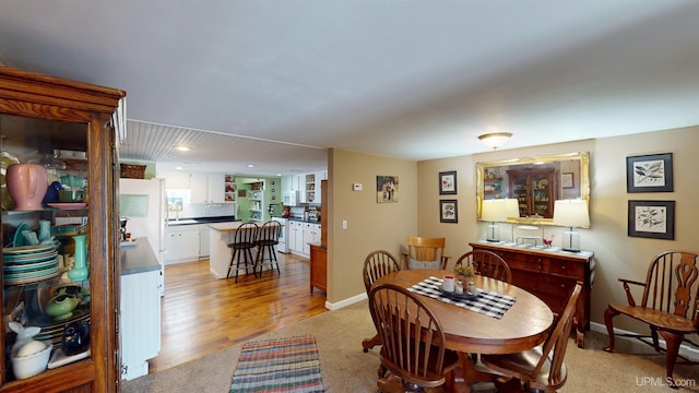 dining space featuring light carpet, light wood-style floors, and baseboards