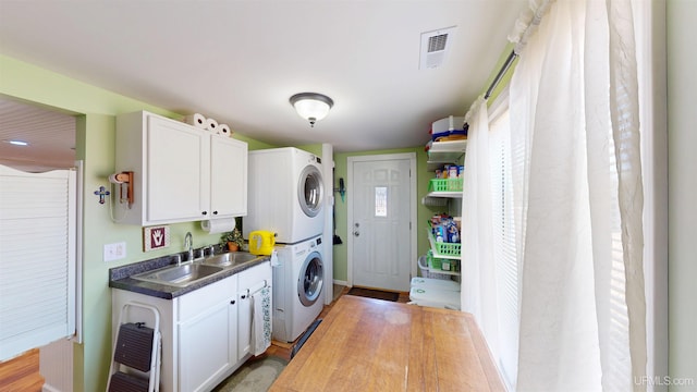 laundry area featuring a sink, cabinet space, baseboards, stacked washer and dryer, and visible vents