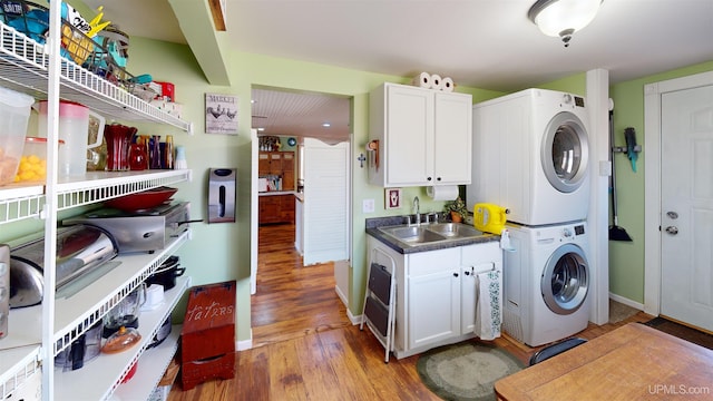 washroom with light wood-style flooring, a sink, baseboards, stacked washer and clothes dryer, and laundry area