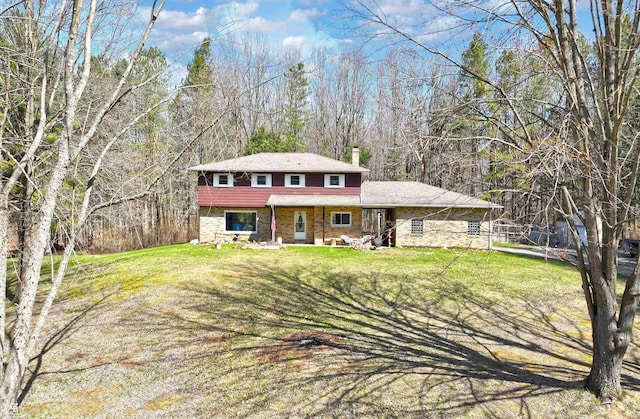view of front of house featuring a front lawn, a chimney, and a view of trees
