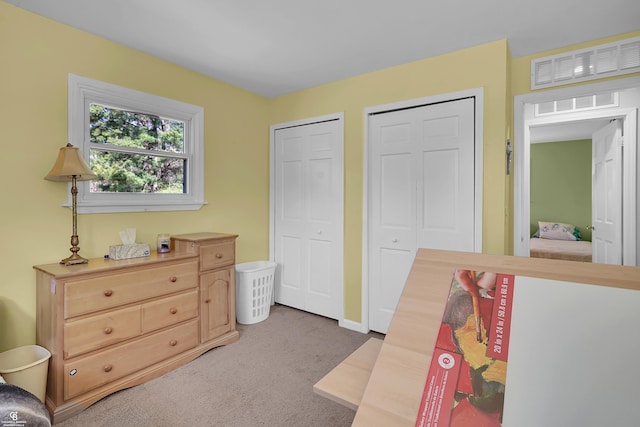 bedroom featuring baseboards, multiple closets, and light colored carpet