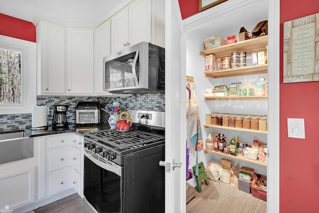 kitchen featuring white cabinets, stainless steel appliances, backsplash, dark countertops, and wood finished floors