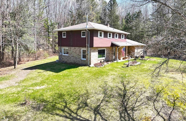 rear view of house featuring a fire pit, stone siding, a chimney, a yard, and a forest view